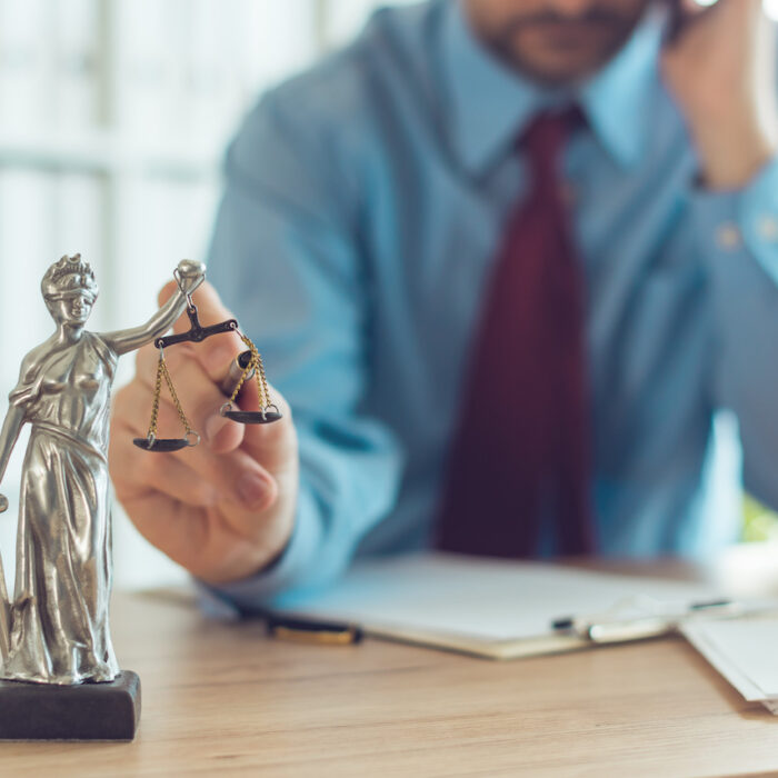 Attorney talking on mobile device and playing with Justice scale in law office, selective focus on statue of Lady Justice