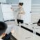 Young sales coach with hair bun wearing glasses holding presentation and explaining graph to business people at training class